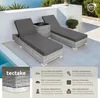 Two grey rattan sun loungers with dark grey cushions are placed on a patio next to a swimming pool. A small rattan side table is between the loungers. The background shows a white wall and some greenery. Náhled obrázku produktu
