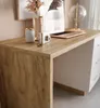 A close-up view of a wooden desk with white drawers, featuring decorative items like a vase with dried flowers, a candle, and a small camera. Produktbild-Vorschau