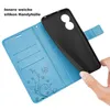 A hand is holding a black phone case over an open blue wallet case with card slots and a floral design. Produktbild-Vorschau