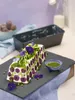 A terrine made with purple potatoes and peas, garnished with flowers and herbs, served on a slate platter with a small bowl of green sauce. Náhled obrázku produktu