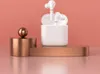 White wireless earbuds in a charging case are displayed on a rose gold pedestal against a pink background. Náhľad obrázku produktu