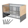A baby crib with wooden accents and loose wooden slats in the foreground, on a white background. Produktbild-Vorschau