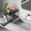 Schwarzer 2-stufiger Schiebe-Organizer, gefüllt mit verschiedenen Toilettenartikeln, auf einem grauen Badezimmerschrank neben einem Waschbecken Anteprima dell’immagine prodotto