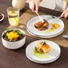 A table setting with plates of food, a salad bowl, and a glass of water, with a person's hands visible. Voir les images du produit