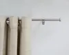 A close-up view of a silver curtain rod with beige curtains hanging from it, mounted on a light gray wall. Produktbild-Vorschau