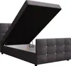 A dark gray upholstered bed frame with the mattress support lifted, revealing storage space underneath. The bed is shown from a side angle against a white background. Náhled obrázku produktu