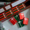 A wooden box containing a Christmas advent calendar with 25 numbered compartments, each with red and green striped paper inserts. Several small gift boxes are scattered in front of the calendar. Náhled obrázku produktu