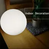 A white spherical lamp sits on a wooden table next to a glass and a patterned cloth. Text overlay indicates 'Indoor Decoration'. Náhľad obrázku produktu