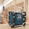 A construction site with wooden beams and scaffolding, where a person is working and a Bosch radio is placed on a wooden surface. Produktbild-Vorschau