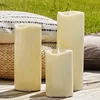 Three LED candles of varying sizes are placed on a wooden deck outdoors, with pillows and grass in the background. Podgląd zdjęcia produktu