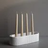 Four beige taper candles stand in a white ribbed oval candle holder against a plain gray background. Produktbild-Vorschau