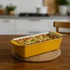 A yellow baking dish filled with food sits on a wooden table in a kitchen. Náhľad obrázku produktu
