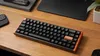 A mechanical keyboard is placed on a wooden desk, with other office supplies in the background. Produktbild-Vorschau
