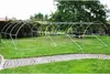 A white metal frame for a greenhouse or tunnel is set up on a green lawn with a paved path in the foreground. Náhľad obrázku produktu