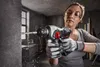 A woman is using a cordless hammer drill to drill into a concrete wall in a workshop or construction setting. Produktbild-Vorschau