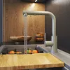 A modern kitchen sink with a faucet running water into the sink, with fruit in a rack and a wooden cutting board in the foreground. Produktbild-Vorschau