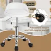 A white office stool with wheels is shown in a studio setting with a blurred background of shelves. Produktbild-Vorschau