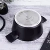 The bottom of a black pot with a silver base is shown on a light-colored wooden surface. A small plant in a black pot is visible to the left, and a black slate with salt is to the right. Podgląd zdjęcia produktu