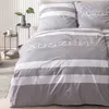 A neatly made bed with grey and white striped bedding, featuring the word 'Auszeit' embroidered on the duvet cover. Produktbild-Vorschau