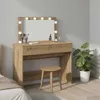 A vanity table with a lighted mirror, makeup brushes, and bottles, next to a potted plant in a room. Voir les images du produit