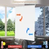 A white roller blind is shown in a window, illustrating temperature regulation with arrows indicating airflow for warm and cold protection. The view outside the window changes from a sunny green landscape to a snowy winter scene. Produktbild-Vorschau