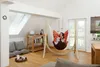 A woman is relaxing in a hammock chair in a bright, airy room with a skylight. Produktbild-Vorschau