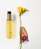 A bottle of hair oil with a yellow flower and a piece of bark with purple flowers. Voir les images du produit