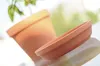 A terracotta plant pot and its saucer are placed on a reflective surface, with a blurred green background suggesting an outdoor or natural setting. Náhľad obrázku produktu