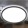 A modern, oval-shaped LED ceiling light with a black frame, mounted on a ceiling in a living room setting. The light is illuminated, casting a soft glow. Náhľad obrázku produktu