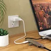 A USB-C adapter hub is connected to a laptop, with a white charging cable plugged into a wall socket. Produktbild-Vorschau