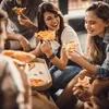A group of friends are sitting together and eating pizza. Anteprima dell’immagine prodotto