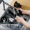A person is cleaning a vacuum cleaner part under a faucet in a sink. Produktbild-Vorschau