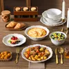 A table setting with a 32-piece stoneware dinnerware set for 8 people, including plates, bowls, and serving dishes, along with food items like croissants, fruit, stew, and honey. Produktbild-Vorschau