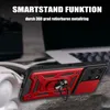A red and black phone case with a ring holder is displayed on a textured surface, with a blurred background of a laptop and headphones. Produktbild-Vorschau