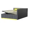 A dark gray upholstered bed frame with the mattress support slats lifted, revealing storage space underneath. Yellow LED lighting is visible along the base and headboard. Produktbild-Vorschau