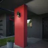 An outdoor wall light with a motion sensor is mounted on a red pillar next to a brick house. Produktbild-Vorschau