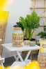 A beverage dispenser and pitcher are on a white table outdoors, with plants and a bamboo screen in the background. Náhled obrázku produktu