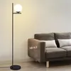 A modern floor lamp with a white globe shade stands next to a brown sofa in a living room. Anteprima dell’immagine prodotto