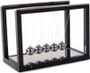 A Newton's cradle toy with silver balls suspended in a black frame, placed on a mirrored surface. Náhľad obrázku produktu