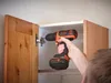 A person is using a Black & Decker cordless drill to attach a cabinet door hinge. Podgląd zdjęcia produktu