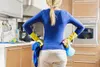A person in a kitchen wearing yellow cleaning gloves and holding cleaning supplies. Náhľad obrázku produktu