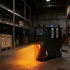A black diesel heater is shown in a warehouse setting, emitting orange heat waves. Voir les images du produit