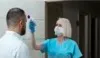 A healthcare worker in blue scrubs and a mask is taking a person's temperature with a non-contact thermometer. Voir les images du produit