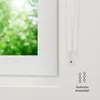 A close-up view of a white window frame with a blurred green background of trees and foliage visible through the window. To the right, a white roller blind mechanism is shown, with a small blue detail and a graphic illustration of three hanging loops with  Anteprima dell’immagine prodotto