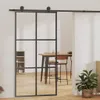 A sliding glass door with a black frame is shown in a room with wooden floors. A dining table and chairs are visible through the glass, and a potted plant is in the foreground. Náhled obrázku produktu