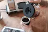 A person pouring coffee from a carafe into a mug next to a coffee maker. Náhľad obrázku produktu