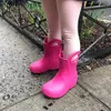 A child's legs wearing pink rain boots standing on a wet sidewalk. Produktbild-Vorschau
