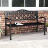 A black metal garden bench sits on a stone patio in front of a brick wall and a window. Podgląd zdjęcia produktu