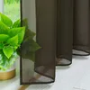 A close-up view of brown sheer curtains with a potted plant in the foreground. Produktbild-Vorschau