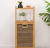 A bamboo shelf unit with decorative items on the shelves and a laundry basket compartment. Náhľad obrázku produktu